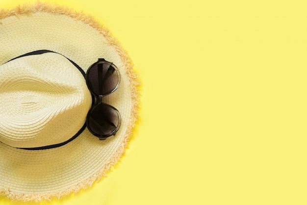 Photo chapeau de foman de plage de paille et lunettes de soleil noires sur fond jaune.