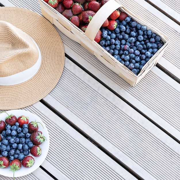 Un chapeau et des fraises et des bleuets frais se trouvent dans un panier