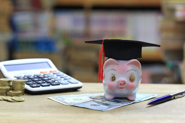 Chapeau de graduation sur tirelire sur étagère dans le fond de la salle de bibliothèque Économiser de l'argent pour le concept d'éducation