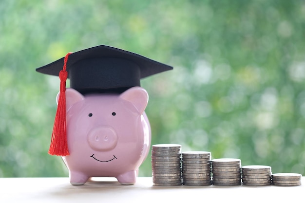 Chapeau de graduation sur tirelire avec pile de pièces d'argent sur fond vert naturel Économiser de l'argent pour le concept d'éducation