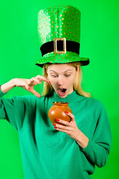 Le chapeau haut de forme vert a surpris une fille en costume de lutin tient un pot avec un pot de lutin en or avec de l'or