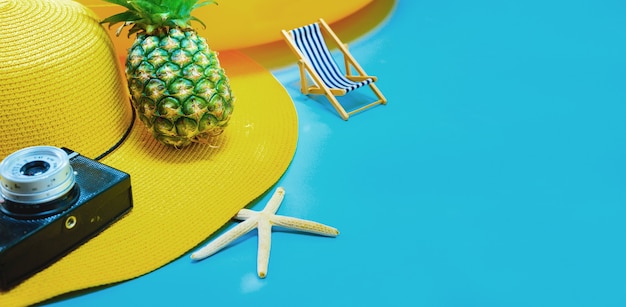 Chapeau jaune avec appareil photo et ananas sur fond bleu pour les vacances d'été.