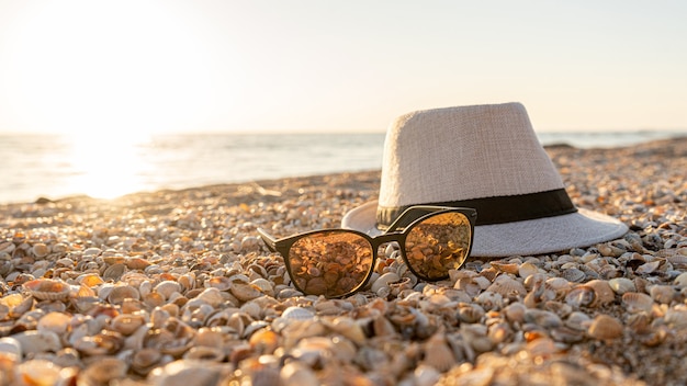 Photo chapeau, lunettes de soleil sur la plage avec une coquille sur un coucher de soleil