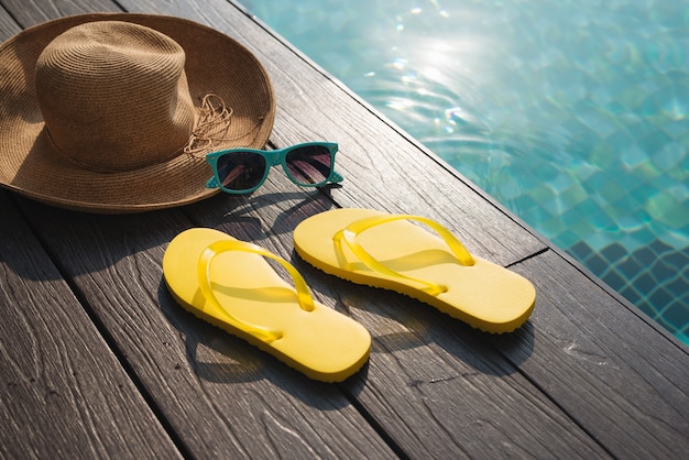 Chapeau, lunettes de soleil et tongs au bord de la piscine