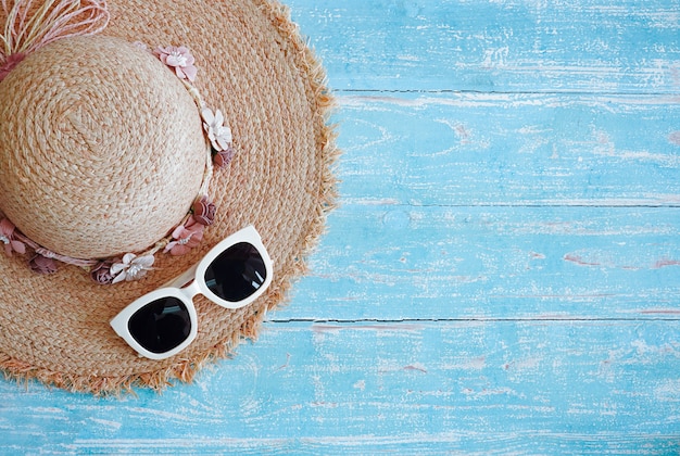 Chapeau de mode et lunettes pour voyager sur fond de bois bleu.