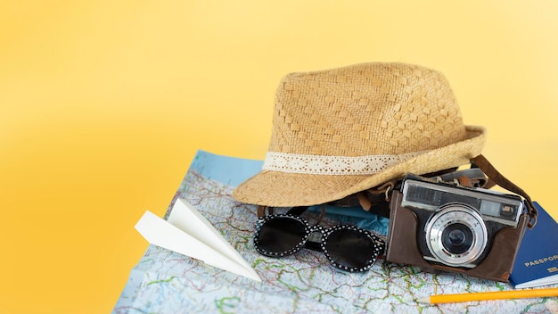 Chapeau de paille, appareil photo argentique vintage, lunettes de soleil sur une carte ouverte sur fond jaune