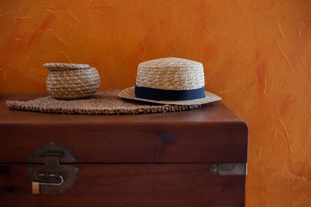 Le chapeau de paille et la boîte de paille sont sur un coffre en bois près du mur orange. Concept de voyage et d'éco
