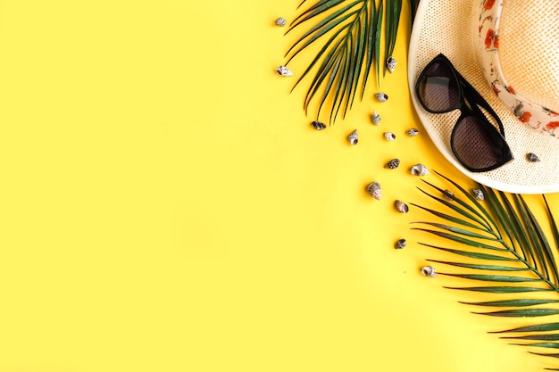 Chapeau de paille, branches de palmier et lunettes de soleil sur fond jaune Vue supérieure Concept de voyage Espace de copie