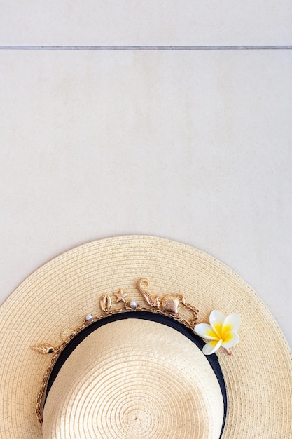 Chapeau de paille avec un collier de coquillages et de perles et la fleur plumeria sur le sol carrelé