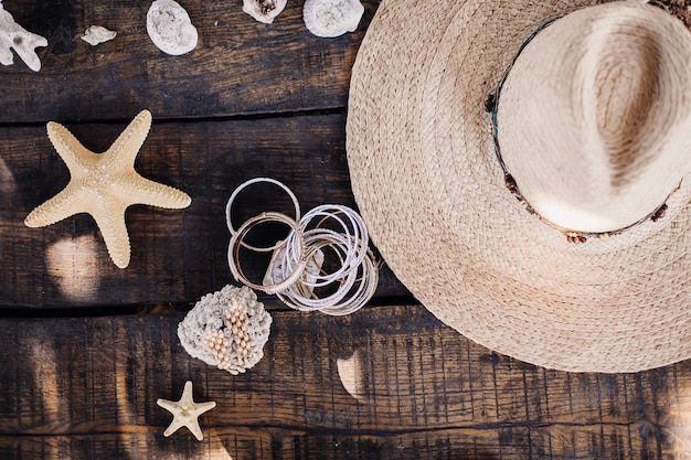 Photo chapeau de paille, coquillages et étoiles de mer sur une table en bois