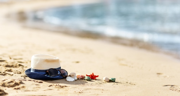 Chapeau de paille, coquillages et lunettes de soleil sur une plage tropicale, espace de copie