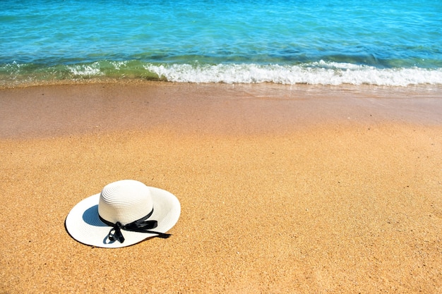 Chapeau de paille femme blanche portant sur la plage de sable tropicale avec de l'eau de l'océan bleu vibrant en arrière-plan sur la journée d'été ensoleillée Vacances et concept de voyage de destination.