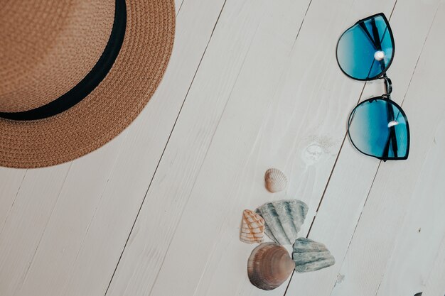 Chapeau de paille et lunettes de soleil bleues sur fond blanc