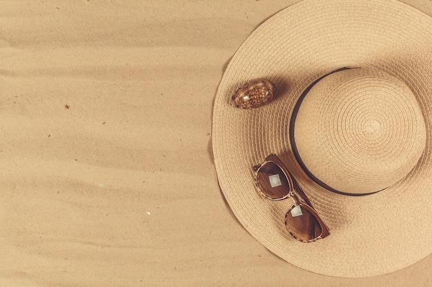 Chapeau de paille et lunettes de soleil sur fond de sable, concept de vacances d'été