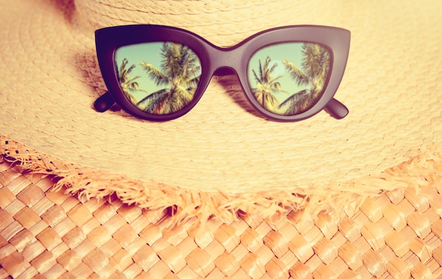 Chapeau de paille avec des lunettes de soleil à la mode noires avec reflet des paumes sur un sac en paille.