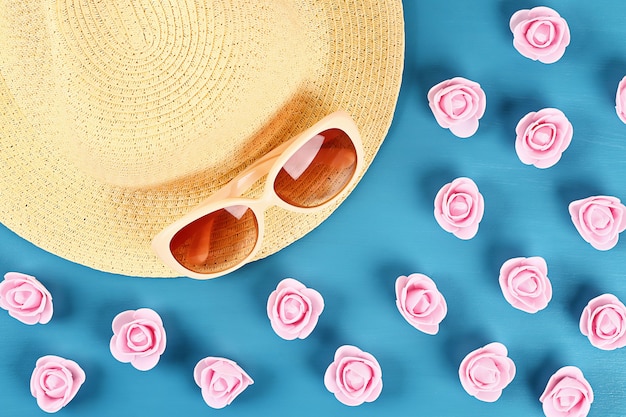 Chapeau de paille et lunettes de soleil avec petites roses sur fond bleu. Vue de dessus. Fond d&#39;été. Pose à plat