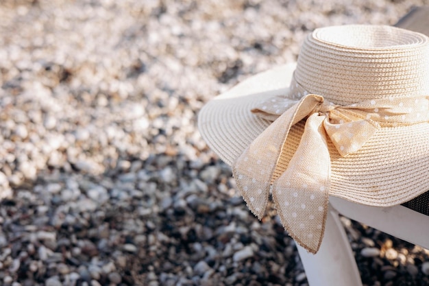 Chapeau de paille pour femme avec noeud sur fond de plage de galets. Concept de vacances, vacances et voyage d'été. Espace de copie