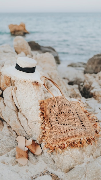 Un chapeau de paille et un sac tissé sur un fond d'écran de téléphone portable sur une plage rocheuse