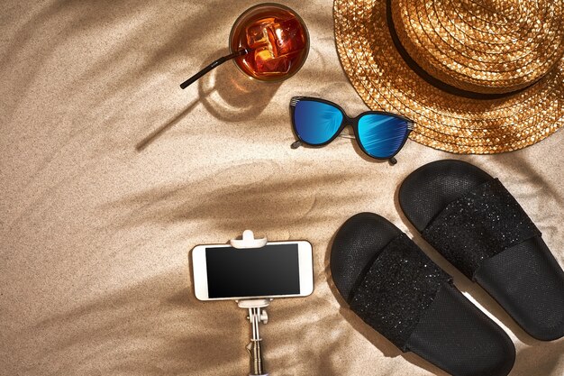 Chapeau de paille sandale et lunettes de soleil sur une vue de dessus de fond de sable