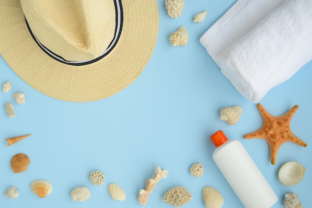 Chapeau de paille de serviette de plage d'étoile de mer de coquillages et crème solaire sur un fond bleu. Concept de vacances d'été