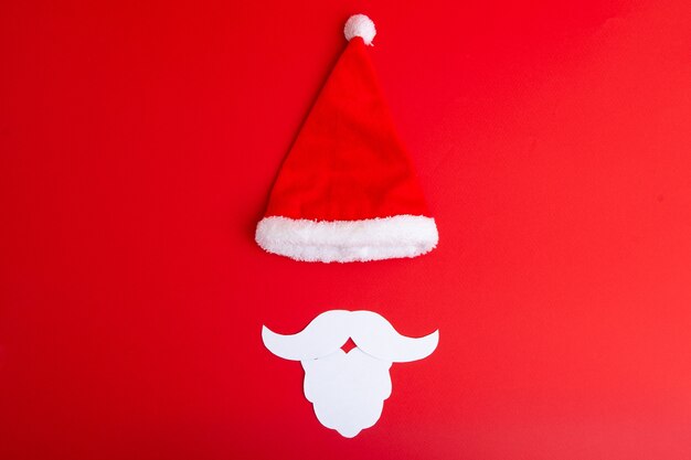 Chapeau de père Noël avec barbe blanche sur fond rouge, mise à plat.
