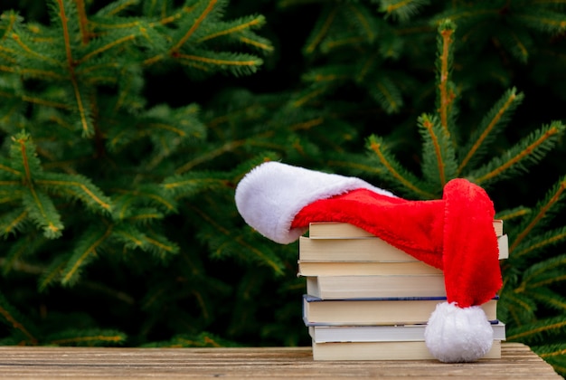 Chapeau de père Noël et livres sur table en bois avec des branches d'épinette sur fond