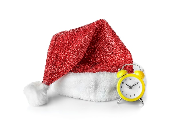 Chapeau de père Noël et petite horloge sur une surface blanche