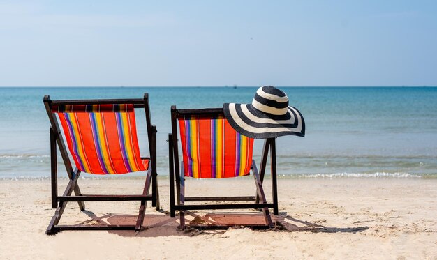 Photo chapeau de plage à rayures bleues et blanches chaise de plage deux chaises de plage sur la plage de sable tropical vacances d'été et concepts de vacances d'été