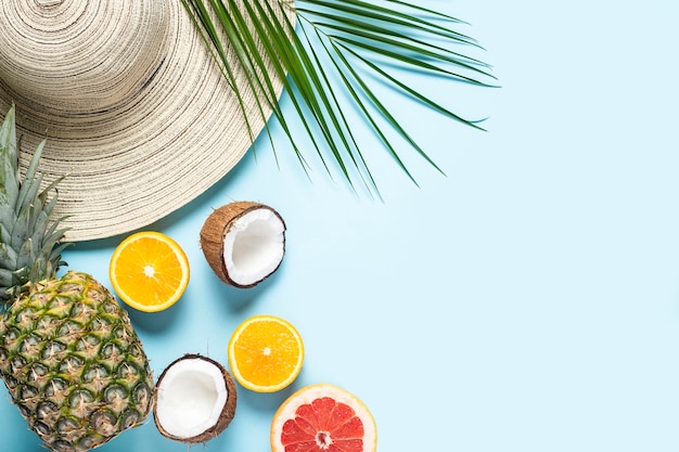 Chapeau pour femme à large bord, fruits tropicaux et branche de palmier sur fond bleu.