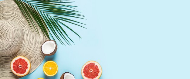 Chapeau pour femme à large bord, fruits tropicaux et branche de palmier sur fond bleu.