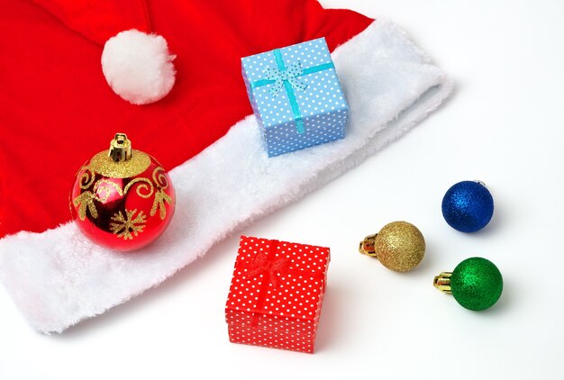 Chapeau rouge et blanc du père Noël, bulles de jouets et cadeaux de Noël sur fond blanc.