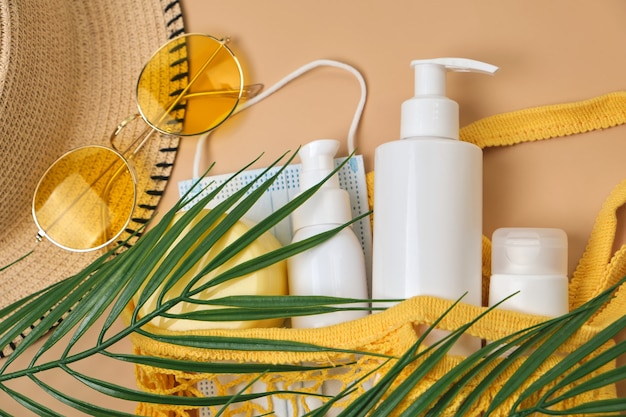 Chapeau de soleil seau, crème de protection solaire SPF dans un sac à cordes, lunettes de soleil et masque sur une surface de sable beige