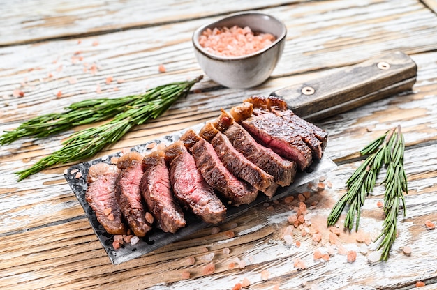 Chapeau de surlonge grillé ou steak de picanha sur un couperet à viande aux herbes. Fond en bois blanc. Vue de dessus.