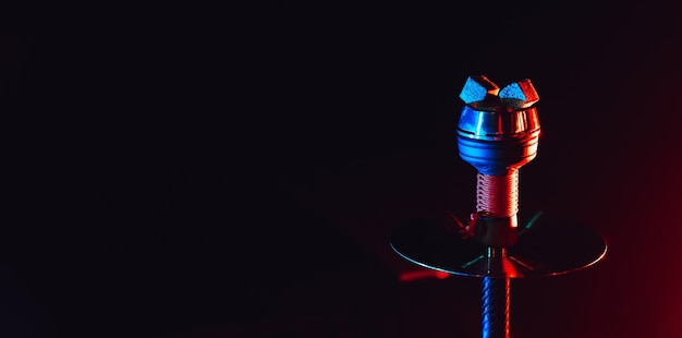 Charbons rouges chauds pour narguilé chicha dans un bol en métal en céramique avec éclairage néon bleu rouge sur fond noir avec un espace de copie