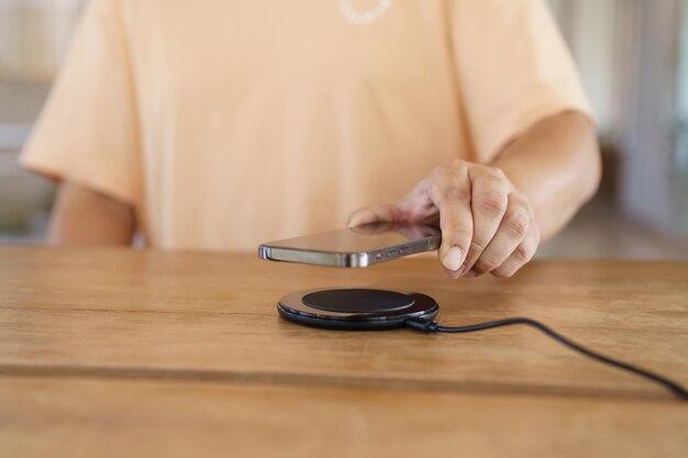 Charge de la batterie du téléphone portable avec un dispositif de charge sans fil dans la table Charge du smartphone sur un socle de charge Téléphone portable près du chargeur sans fil Concept technologique de style de vie moderne