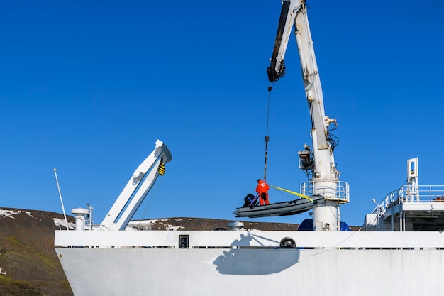 Photo chargement d'un bateau pneumatique avec chauffeur sur le pont à l'aide d'une grue de navire. expédition arctique.