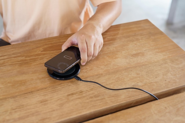 Chargement de la batterie d'un téléphone portable avec un dispositif de charge sans fil dans la table Chargement d'un smartphone sur un chargeur Téléphone portable près d'un chargeur sans fil Concept de technologie de style de vie moderne