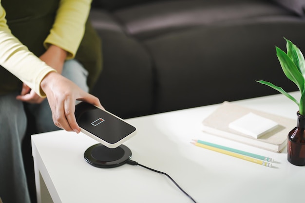 Chargement de la batterie d'un téléphone portable avec un dispositif de charge sans fil dans la table Chargement d'un smartphone sur un chargeur Téléphone portable près d'un chargeur sans fil Concept de technologie de style de vie moderne