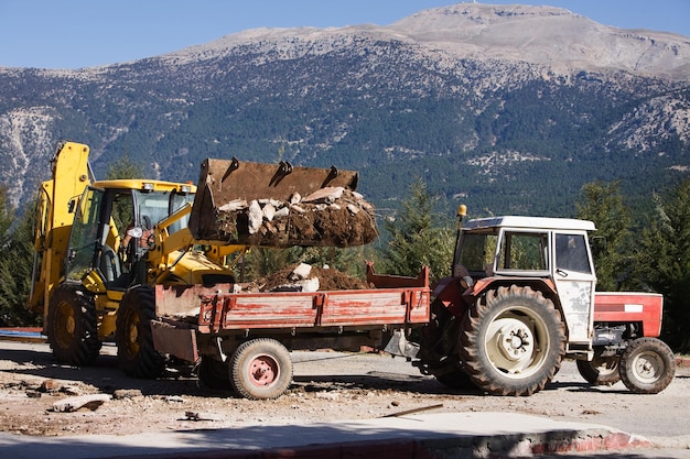 Chargement des décombres de la construction sur le chariot de chargement du tracteur, montagnes du Taurus en arrière-plan, Turquie