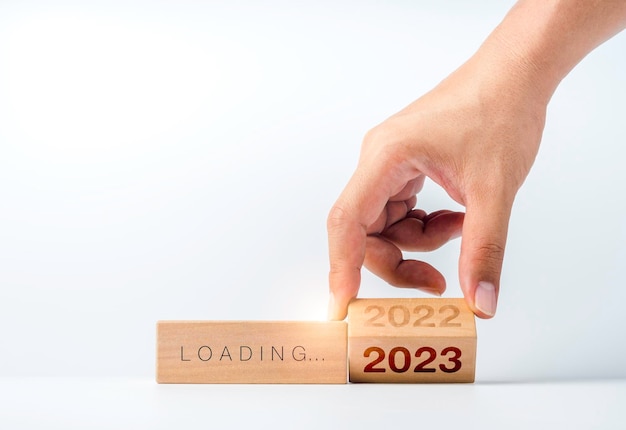 Chargement jusqu'à 2023 bonne année Retourner à la main le calendrier des numéros de l'année 2022 à 2023 sur des blocs de cube en bois isolés sur fond blanc pour se préparer au changement de nouvelle année et démarrer un nouvel objectif commercial