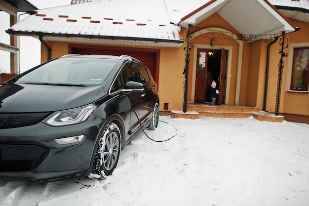 Chargement de la voiture électrique dans la cour de la maison en hiver