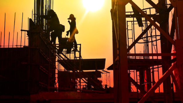 Charges de travail des travailleurs de la construction sur le chantier de construction avec fond de coucher de soleil ciel abstrait
