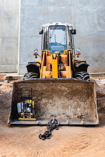 Chargeur frontal lourd sur un chantier de construction avec un outil de construction dans le godet. Equipements pour les travaux de terrassement, le transport et le chargement de matériaux en vrac - terre, sable, pierre concassée.