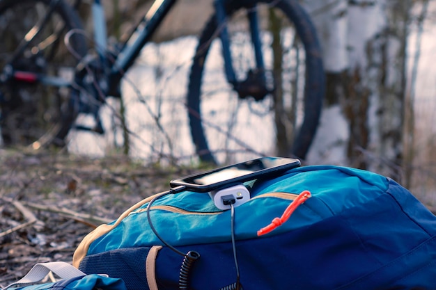 Un chargeur portable charge le smartphone. Banque d'alimentation avec câble sur fond de bois et de vélo.