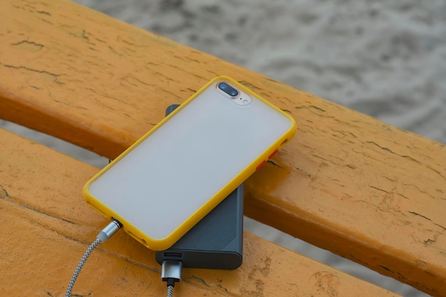 Un chargeur portable charge le smartphone Power Bank avec câble sur fond de banc en bois