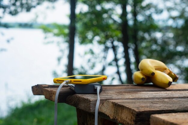 Chargeur de voyage portable. Power Bank charge un smartphone sur une table en bois avec des bananes, sur fond de nature. Concept sur le thème du tourisme.