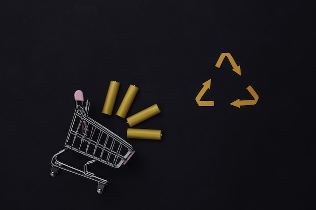 Chariot d'achat avec quatre piles AA jaunes et signe de flèches recyclées sur fond noir. Vue de dessus