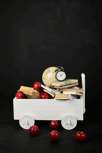 Un chariot blanc avec un globe de livres et des pommes sur un fond noir