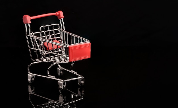 Chariot de caddie rouge gros plan avec réflexion sur fond noir, concept de commerce et de shopping.