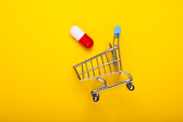 Chariot de supermarché avec capsule de pilule sur fond jaune. Vue de dessus